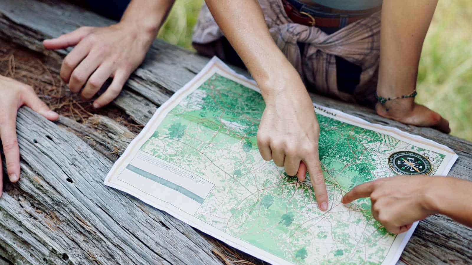 Two people pointing at a detailed topographic map outdoors in a green setting.