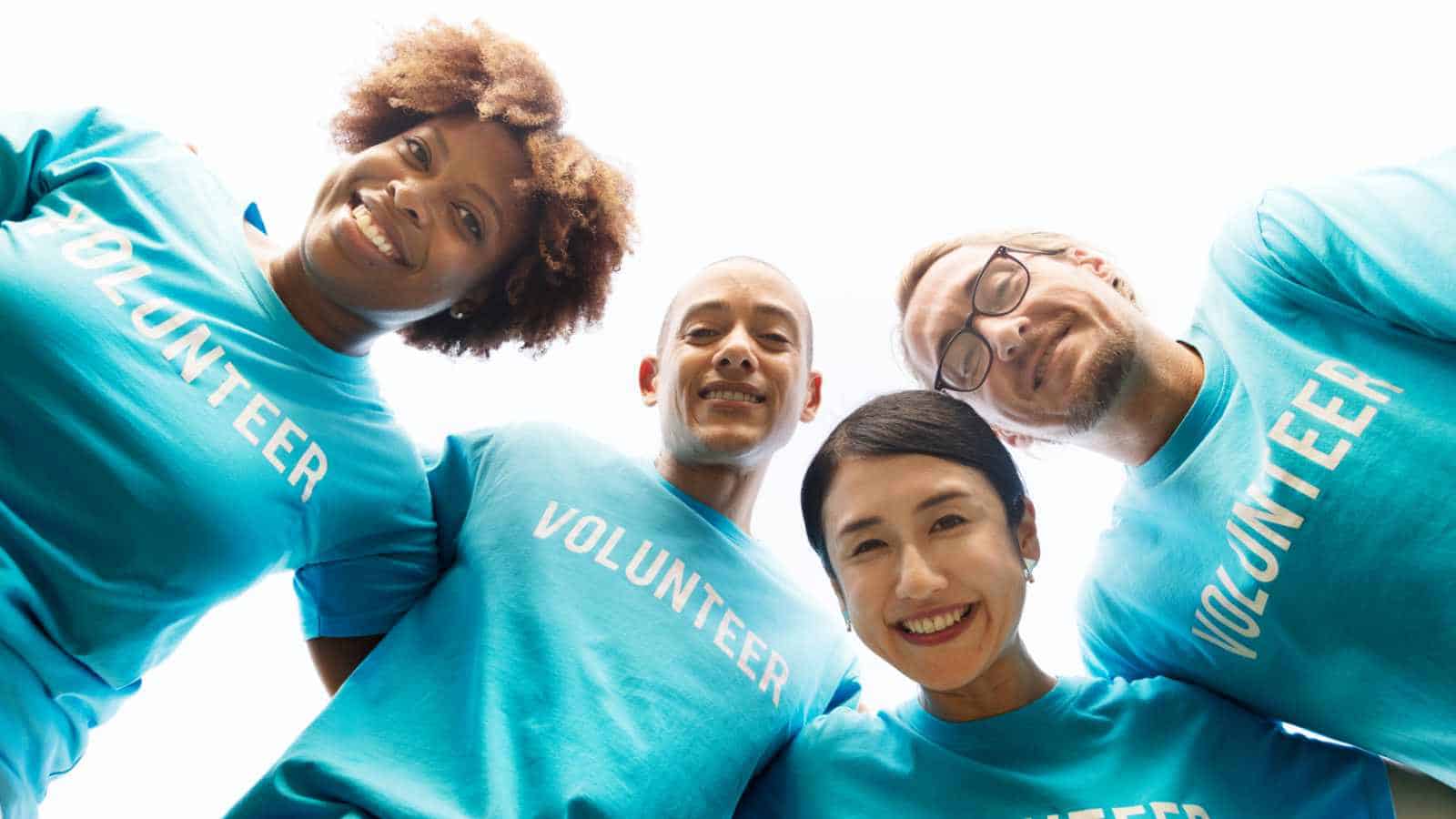 Diverse group of volunteers smiling in blue "Volunteer" shirts outdoors.
